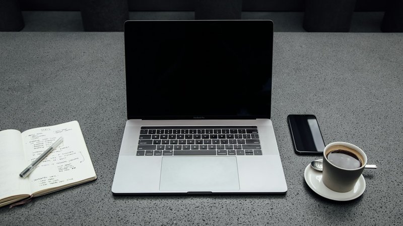 ノートパソコンとメモ帳、コーヒーが置かれたデスク